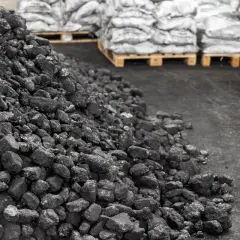 Kupa węgla na placu składowym, w tle worki z węglem na paletach. Zastanawiasz się, ile kosztuje tona węgla?