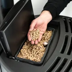 Dłoń wsypuje tani pellet z Czech do zasobnika nowoczesnego pieca.