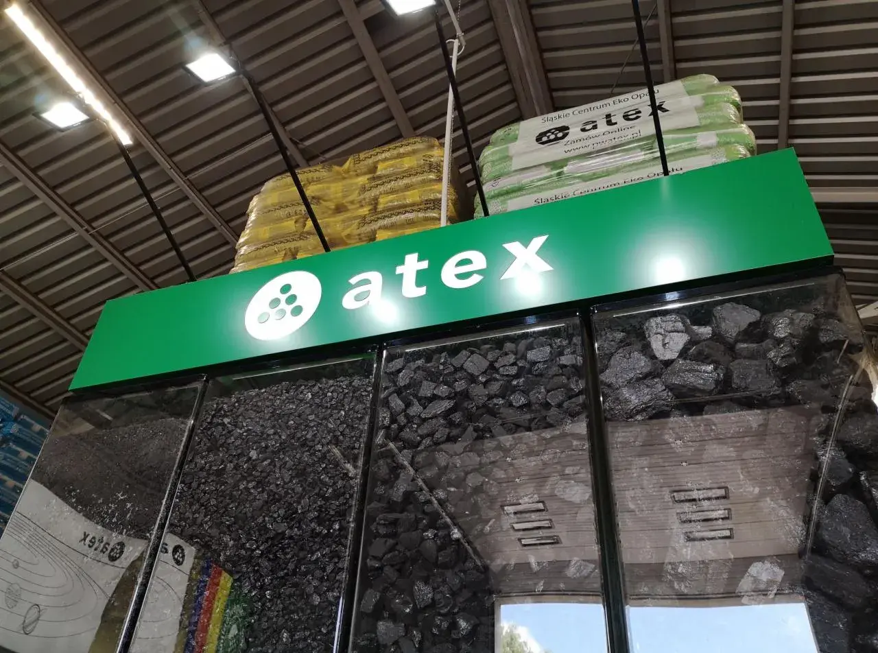 Atex Pilchowice: ceny węgla. Różne rodzaje węgla w gablotach, nad nimi logo Atex i paczki z ekogroszkiem.