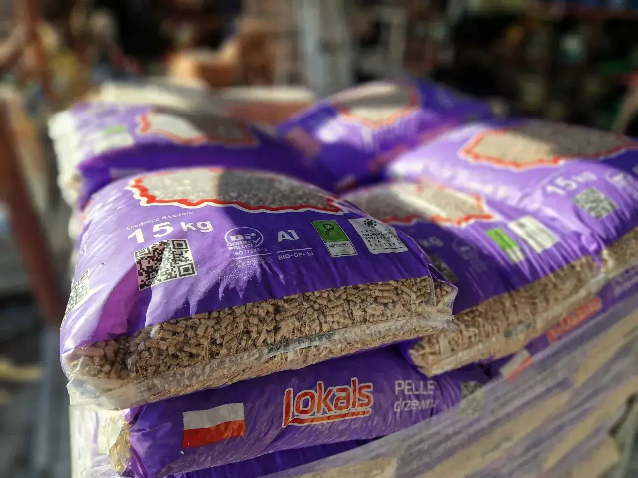 Stos worków z pelletem drzewnym, każdy po 15 kg. W tle widać kolejne palety. Idealne rozwiązanie do ogrzewania, dostępne w Mińsku Mazowieckim.