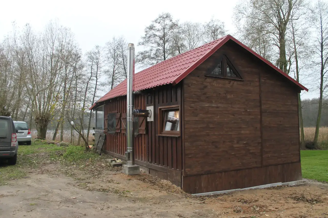 Nowy, błyszczący komin do domku drewnianego, zamontowany na zewnątrz, obok brązowej ściany.